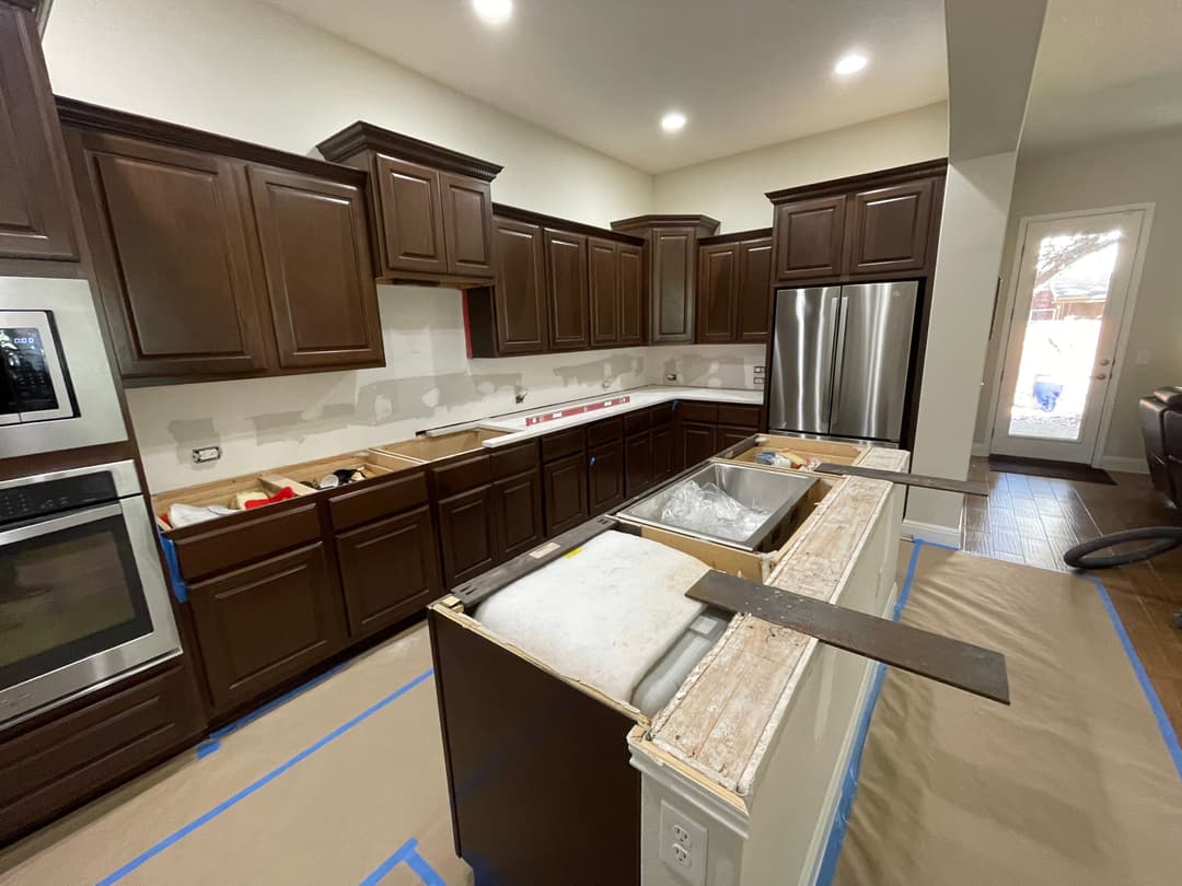 Modern kitchen under renovation with dark cabinets, stainless steel appliances, and uninstalled sink.