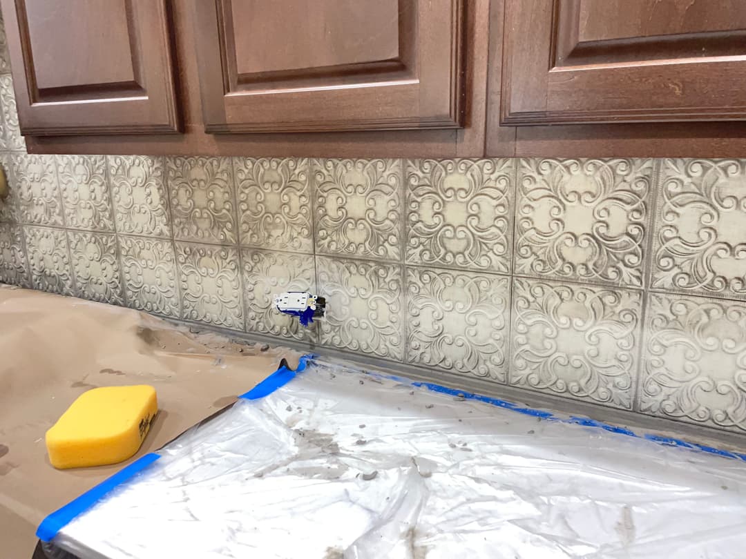 Kitchen backsplash installation with decorative tiles, wooden cabinets, and countertop preparation.