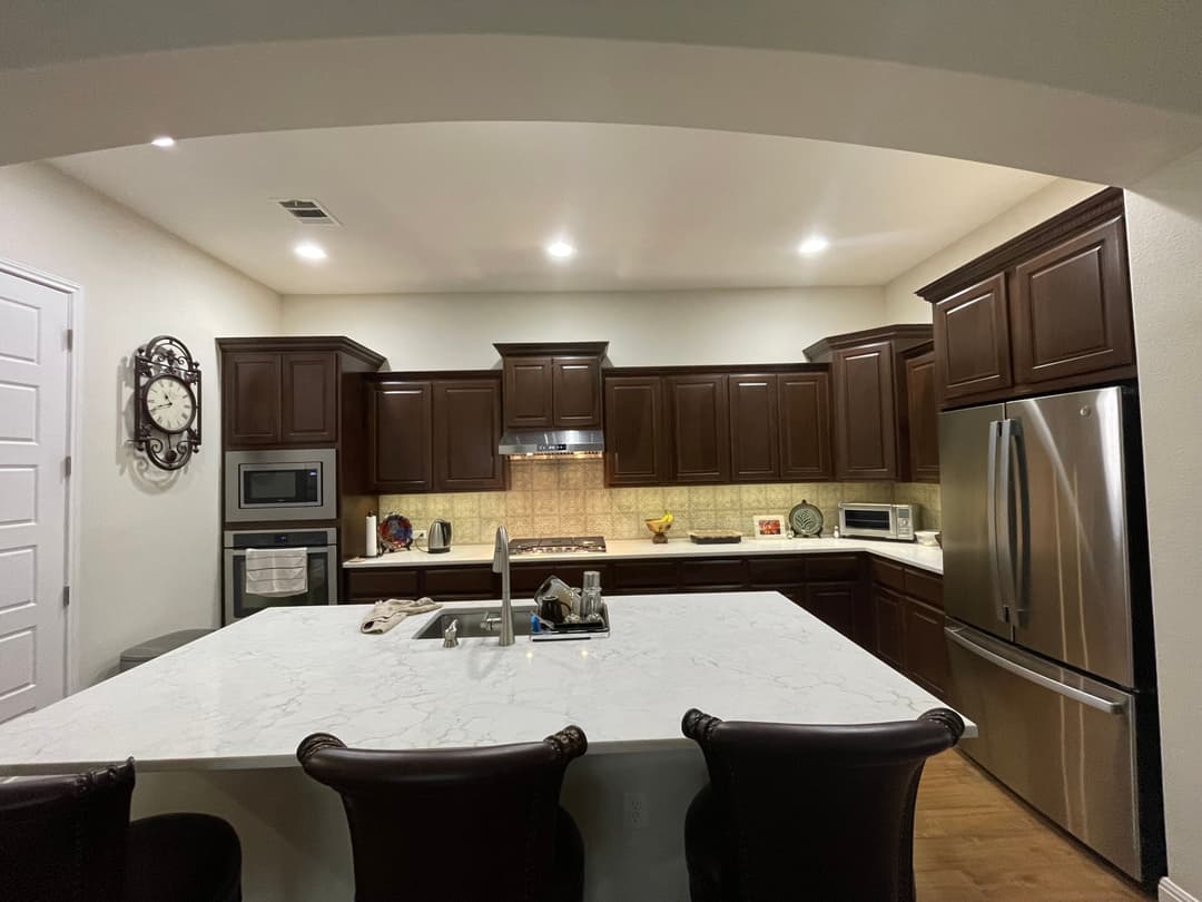 Modern kitchen with dark wood cabinets, marble island, and stainless steel appliances.