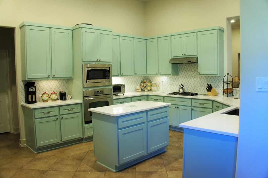 Modern kitchen with light blue cabinets, white countertops, and stainless steel appliances.