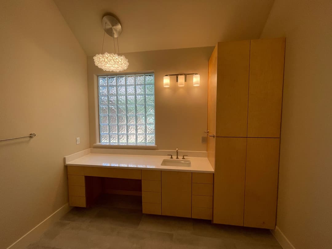 Modern bathroom with a glass block window, light wood vanity, and stylish chandelier.