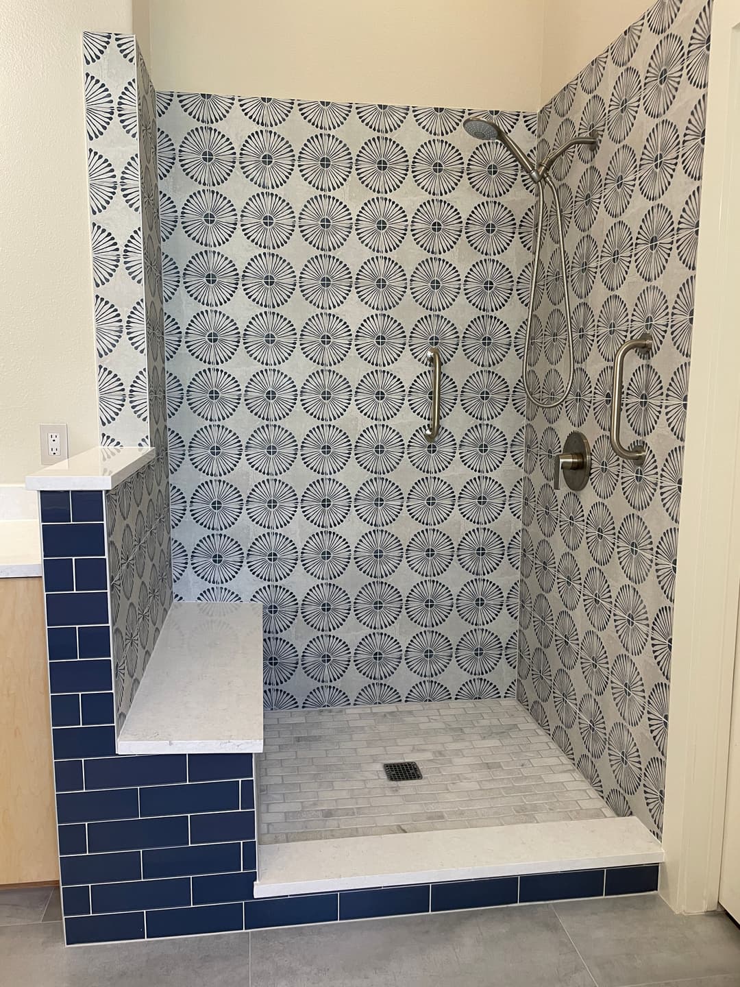 Modern walk-in shower with patterned tiles, grab bars, and a built-in bench.