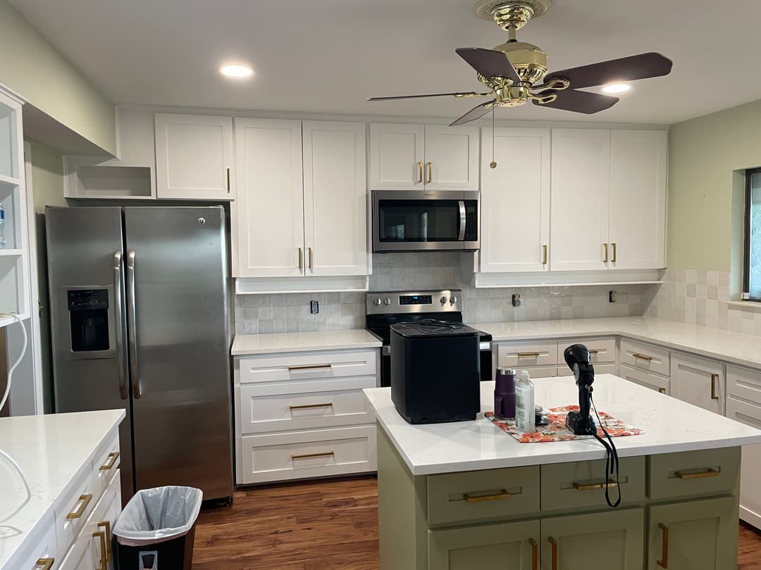 Modern kitchen with white cabinetry, stainless steel appliances, a ceiling fan, and wooden flooring.