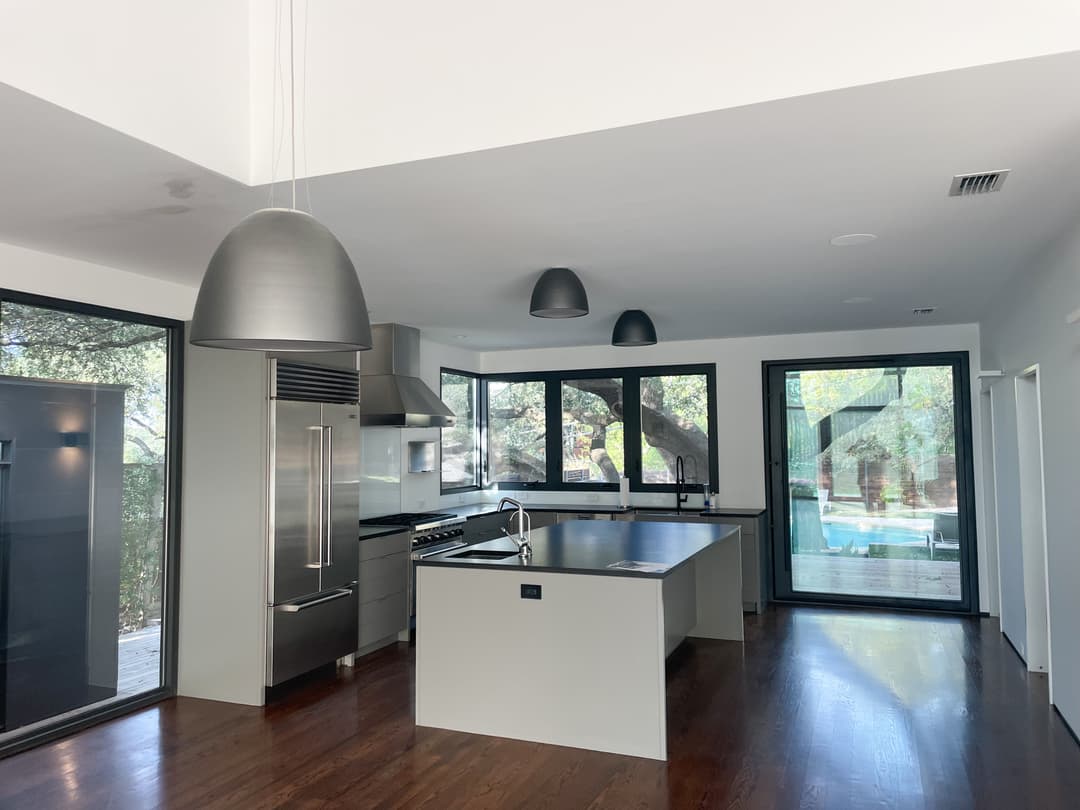 Modern kitchen with stainless steel appliances, large windows, and wooden flooring.