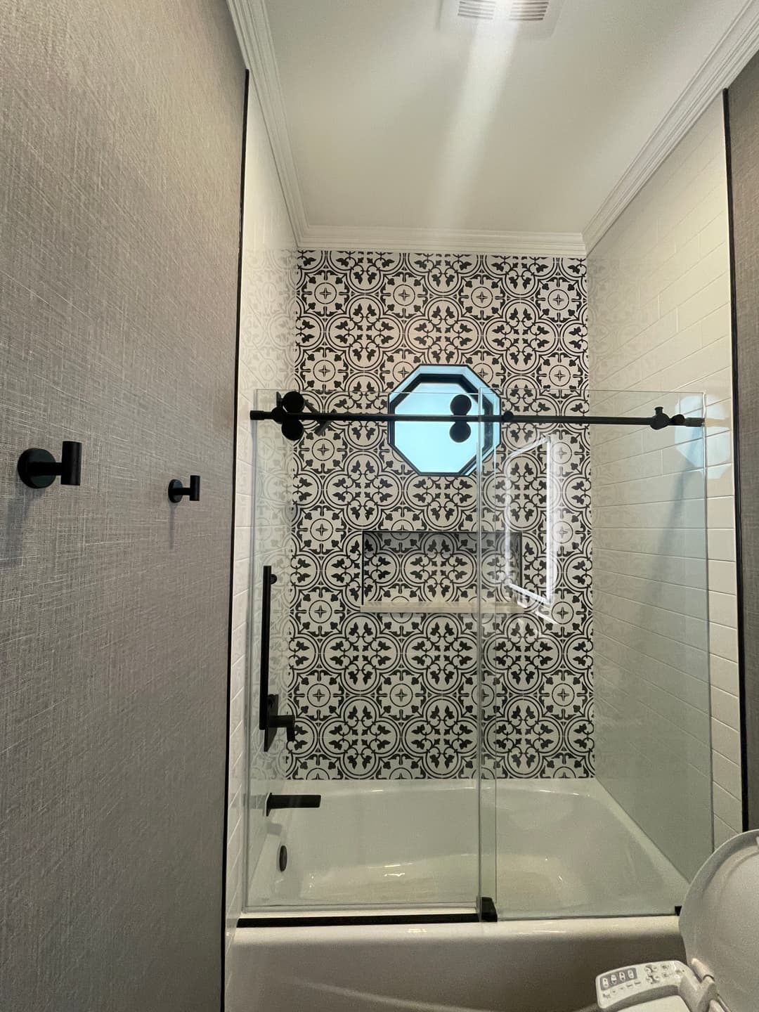 Modern bathroom with decorative tile wall, sliding glass shower door, and stylish black fixtures.