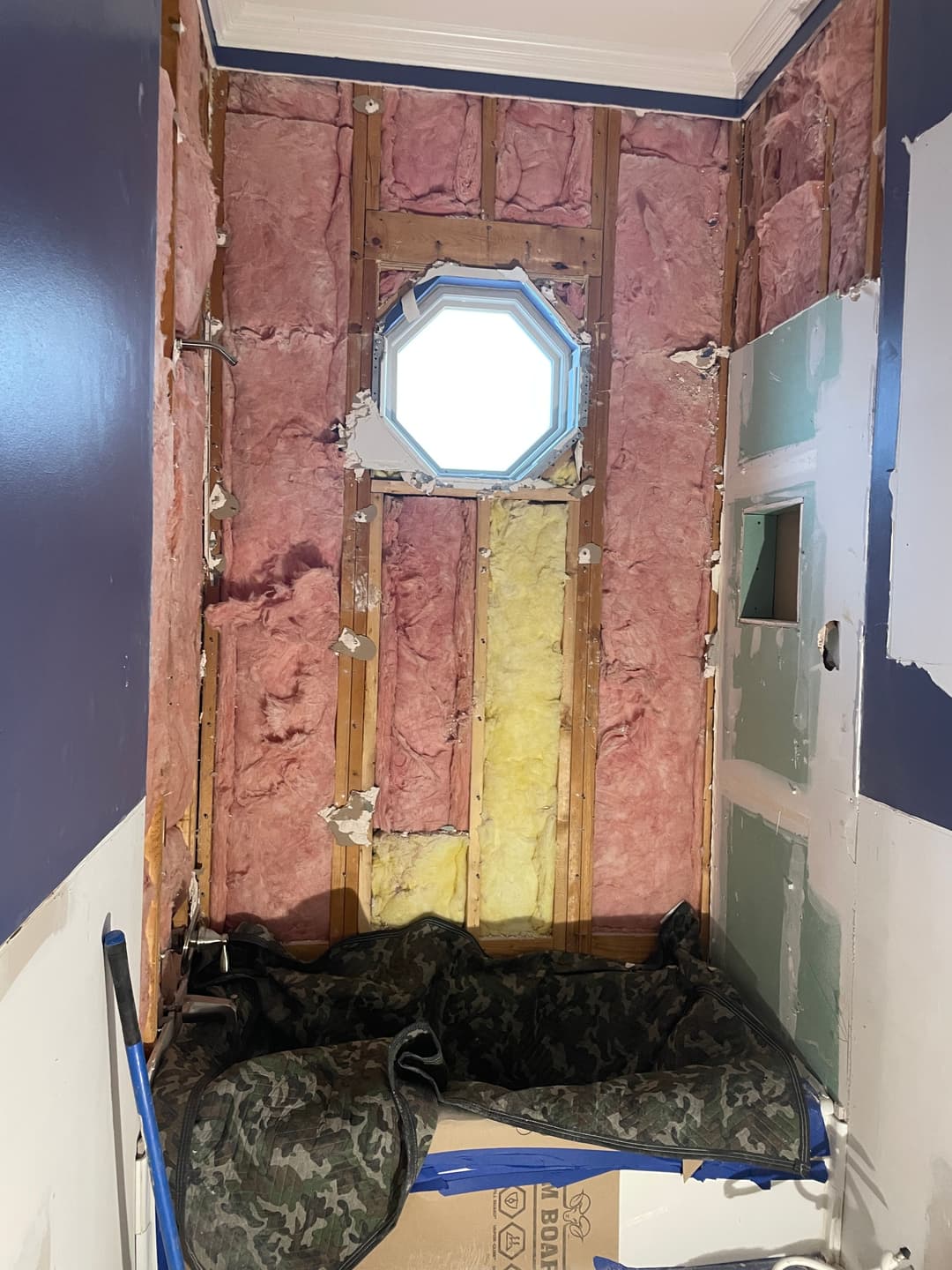 Insulation exposed in a room renovation, featuring wooden studs and an octagonal window.