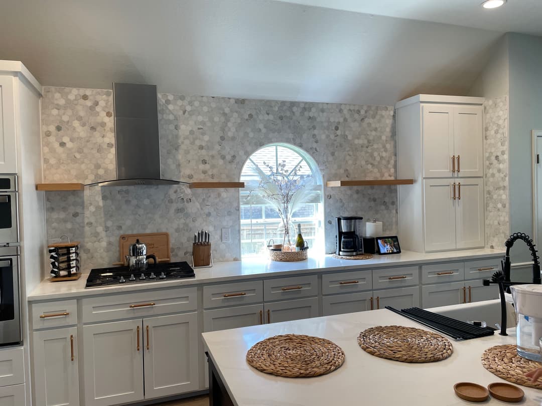 Modern kitchen with gray and white mosaic backsplash, stainless steel hood, and light wood accents.