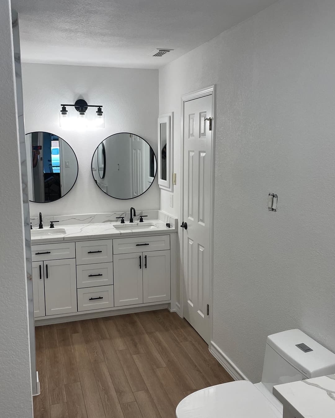 Modern bathroom with double mirrors, white cabinetry, and wood-look flooring.