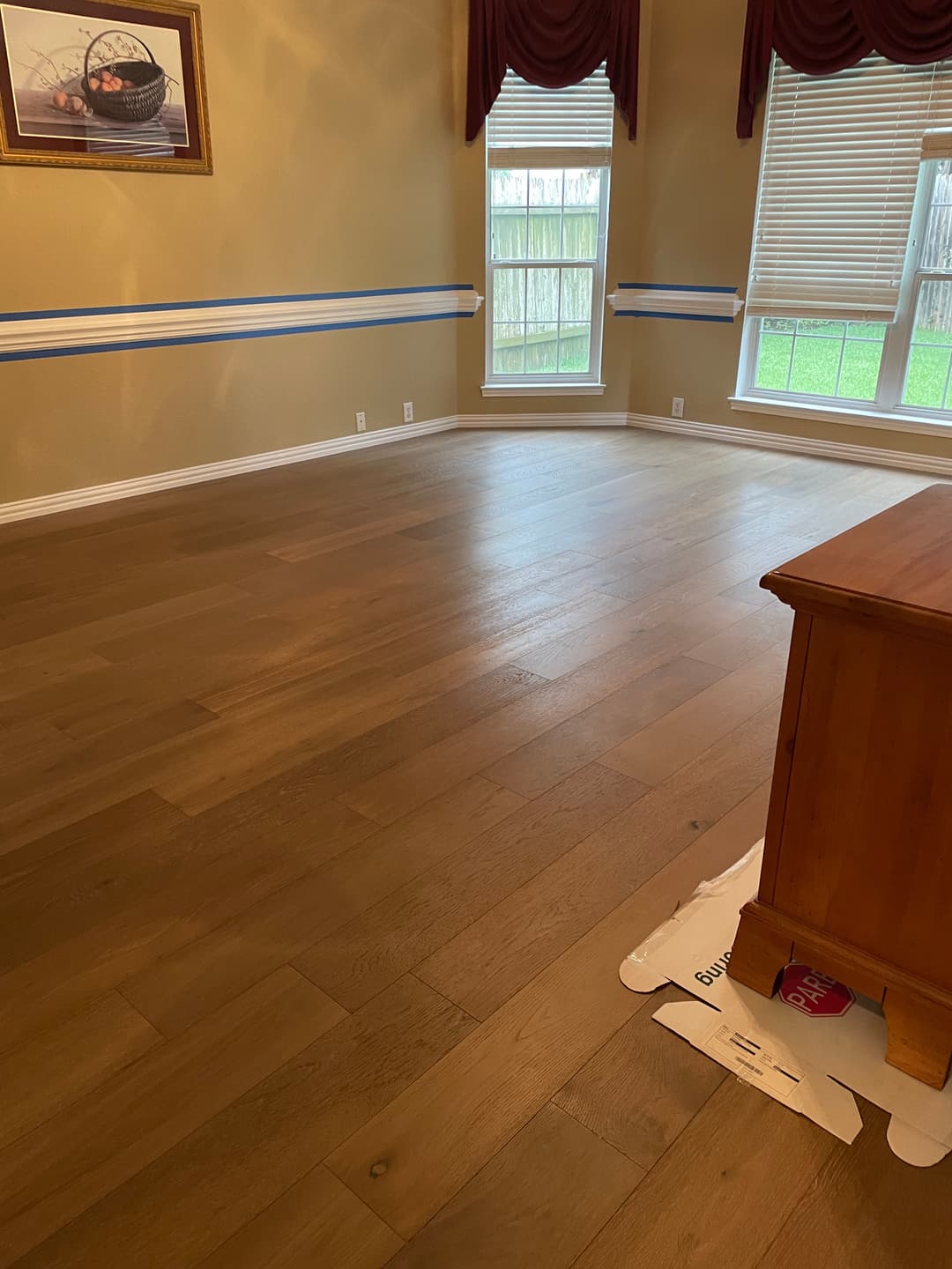 Empty room with hardwood flooring, large windows, and beige walls.