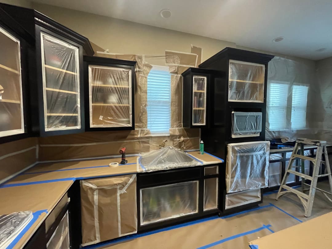 Kitchen undergoing renovation with black cabinets covered in plastic and painter's tape.